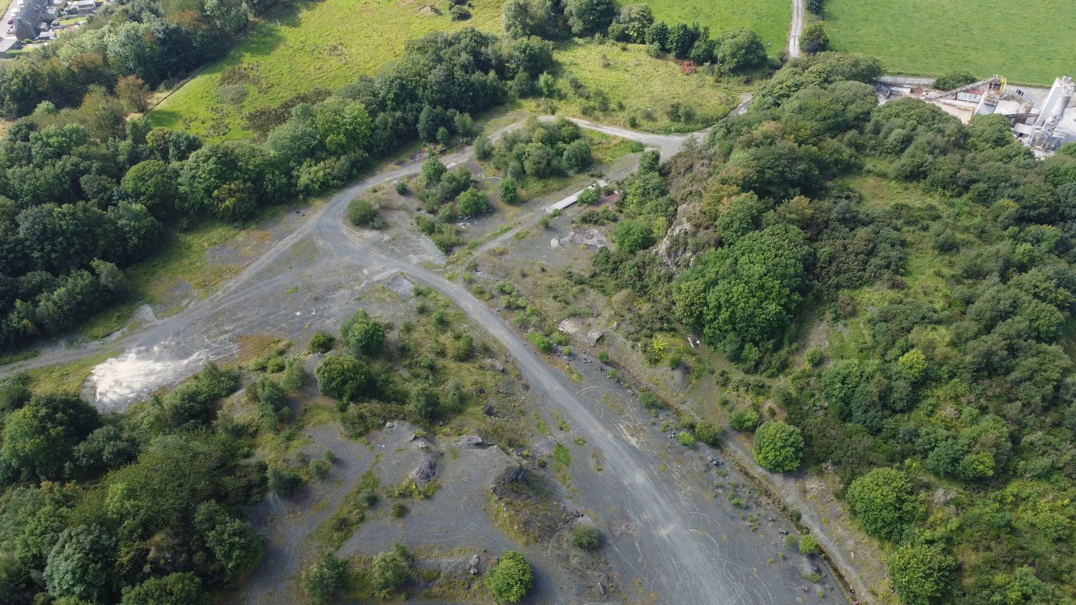 Drone view of a quarry site of bare, disturbed ground with tracks and ponds.