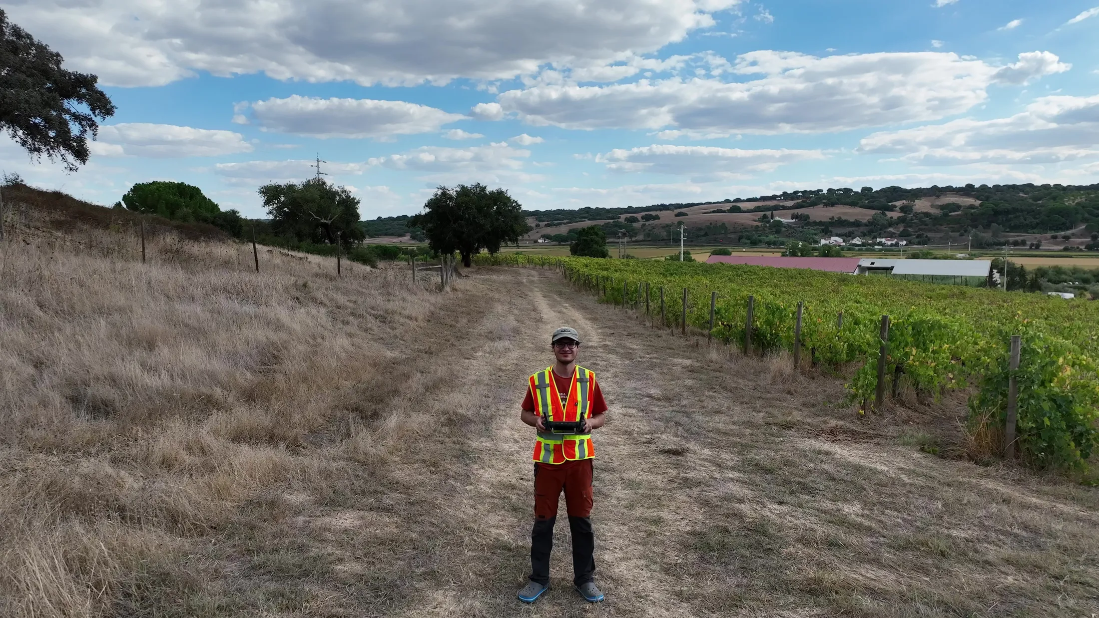 Leonluca Klein holding a drone controller on a dirt track beside a vineyard.