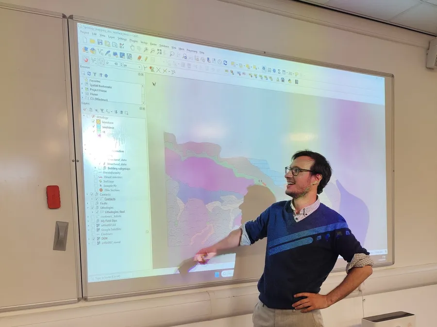 Leonluca Klein pointing at a geological map in QGIS projected on a classroom screen.